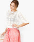 A woman wearing a white short-sleeve crochet knit top with a geometric openwork pattern and a pink floral print skirt, posed against a clean white background.