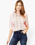 A woman wearing a light pink open-knit short-sleeve top with a geometric pattern, paired with dark blue jeans, against a plain white background.