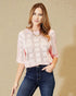 Woman wearing a pink lace top and blue jeans against a beige background