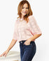 A woman wearing a light pink open-knit short-sleeve top and dark blue jeans, posing against a clean white background.