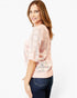 A woman modeling a light pink open-knit sweater with three-quarter sleeves and a ribbed hem, paired with dark blue jeans against a plain white studio background.