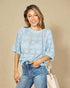 Woman wearing a light blue crochet top and jeans, standing against a beige background