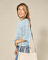 Woman wearing a light blue sweater and holding a beige handbag against a beige background