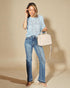 Woman wearing a light blue top and jeans, holding a beige handbag against a beige background