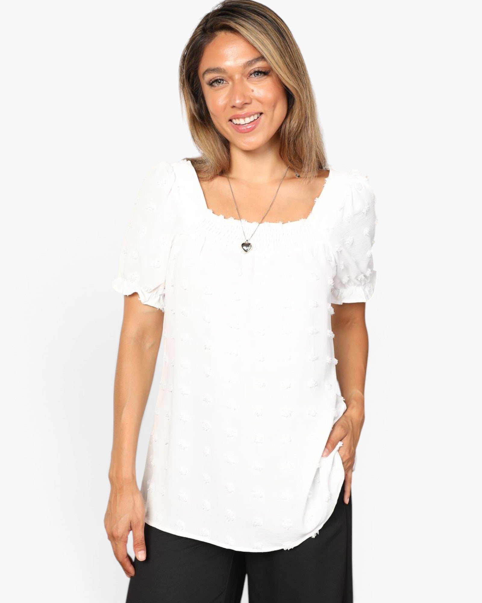 A woman wearing a white short-sleeve top with a square neckline and textured fabric, paired with black pants, against a plain white background.