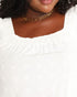 Close-up of a person wearing a white textured top with a smocked neckline and a gold chain necklace.