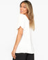 A woman wearing a white short-sleeve top with textured ruffles, paired with black pants, photographed against a plain white studio background.