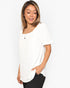 A woman wearing a white short-sleeve tunic top with a scalloped neckline and textured dot pattern, paired with black pants, against a plain white background.