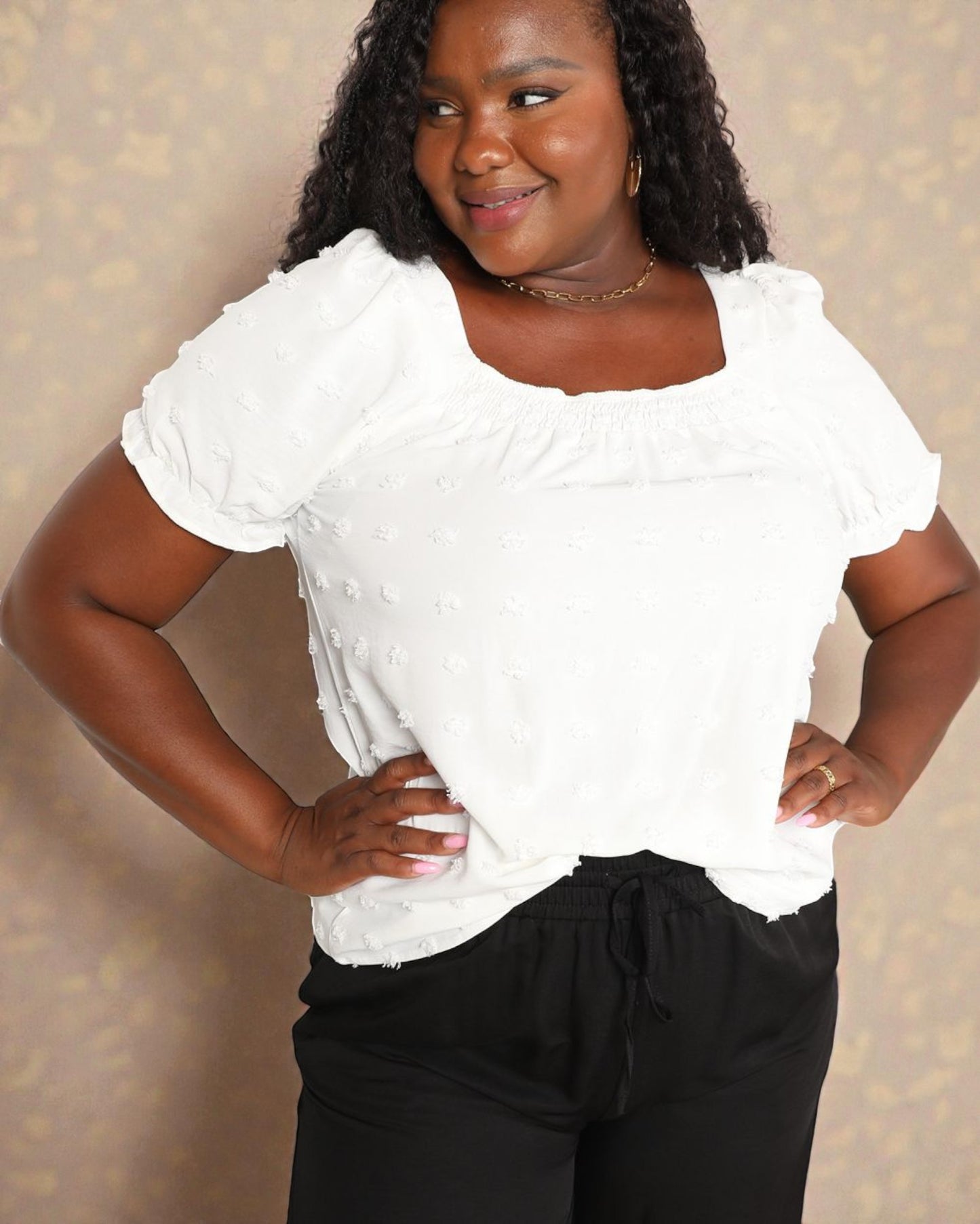 Woman wearing a white textured top and black pants against a neutral background