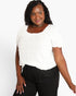 A woman wearing a white short-sleeve puff-sleeve top with a square neckline and black pants, standing against a light gray studio background.