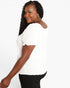 A woman wearing a white short-sleeve top with textured puff sleeves and black pants, photographed against a plain white studio background.