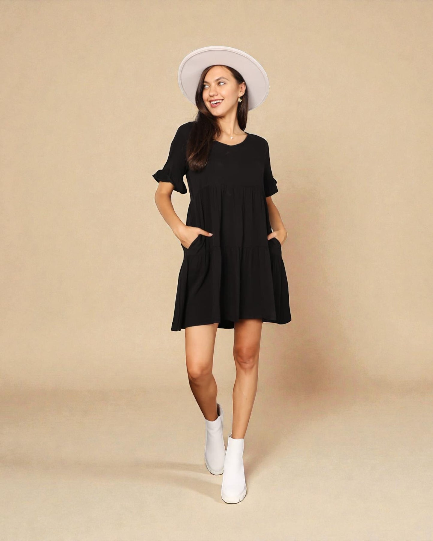 Woman wearing a black dress and white hat on a beige background