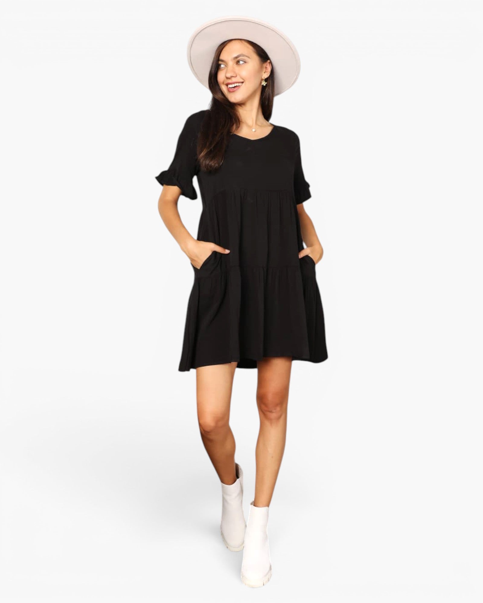 A woman modeling a black short-sleeve mini dress with ruffled sleeves and front patch pockets, styled with a light beige wide-brim hat and white ankle boots against a plain white studio background.