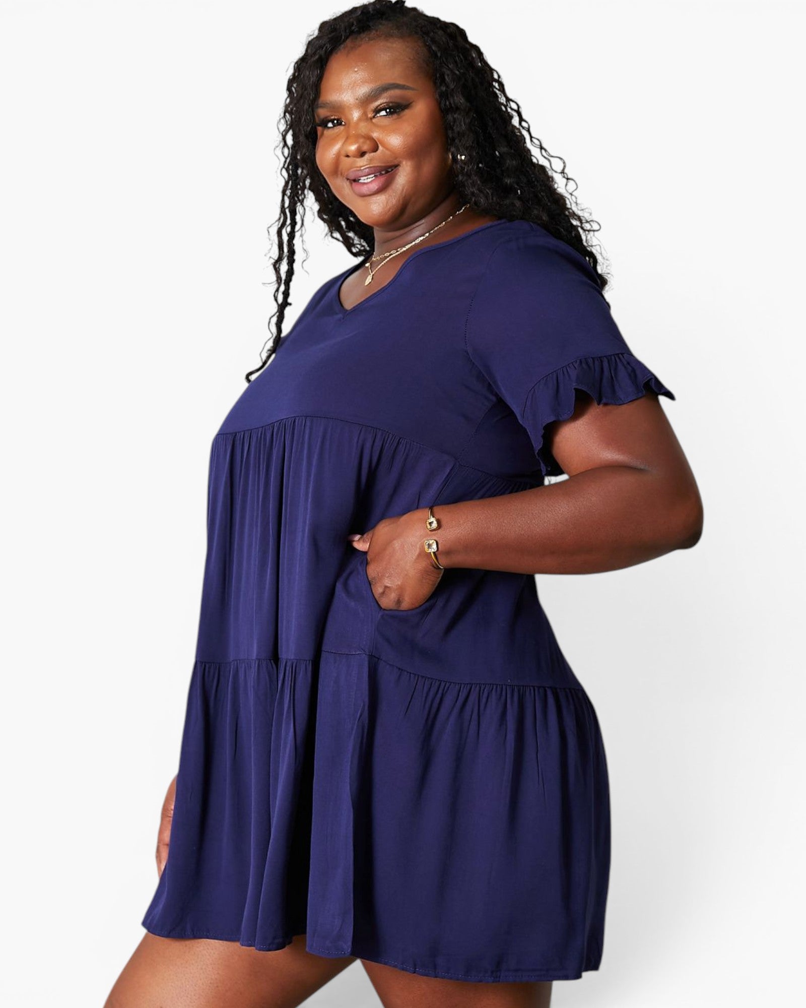 A woman modeling a short-sleeve tiered mini dress in a deep purple color, standing against a plain white studio background.