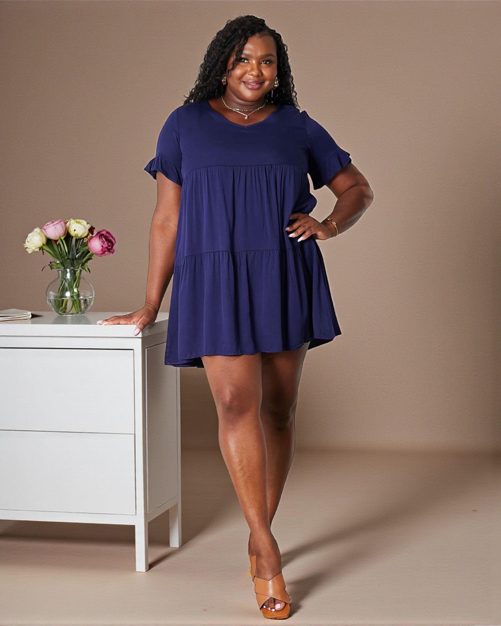 Woman in a blue dress standing next to a white cabinet with flowers on it.