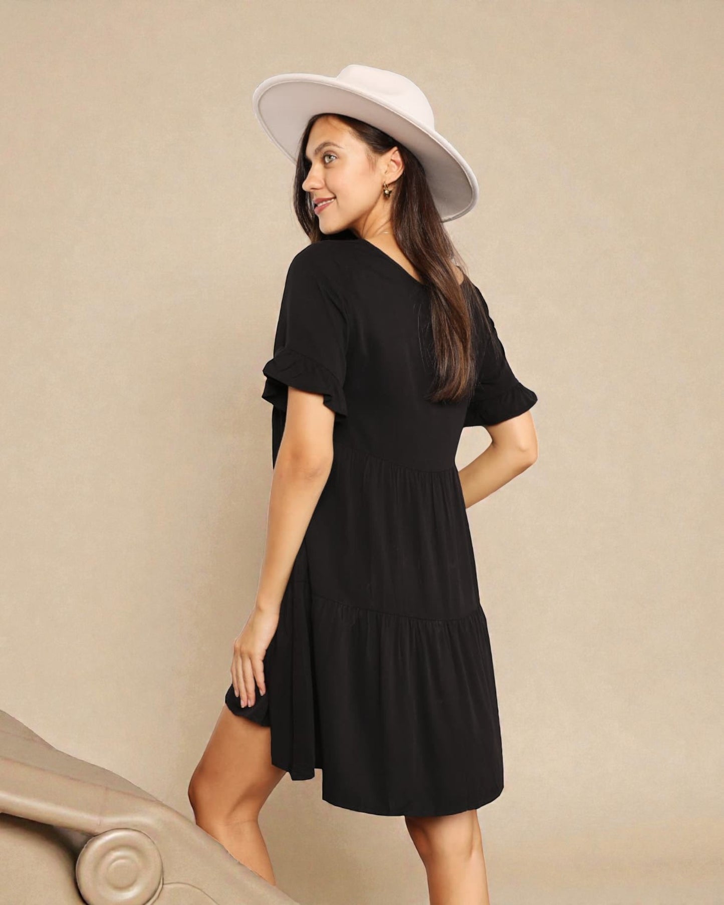 Woman wearing a black dress and white hat against a beige background