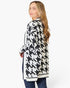 A woman modeling a black and white houndstooth pattern cardigan, shown from a side-back angle against a plain white studio background.