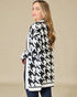 Woman wearing a black and white houndstooth patterned cardigan against a beige background