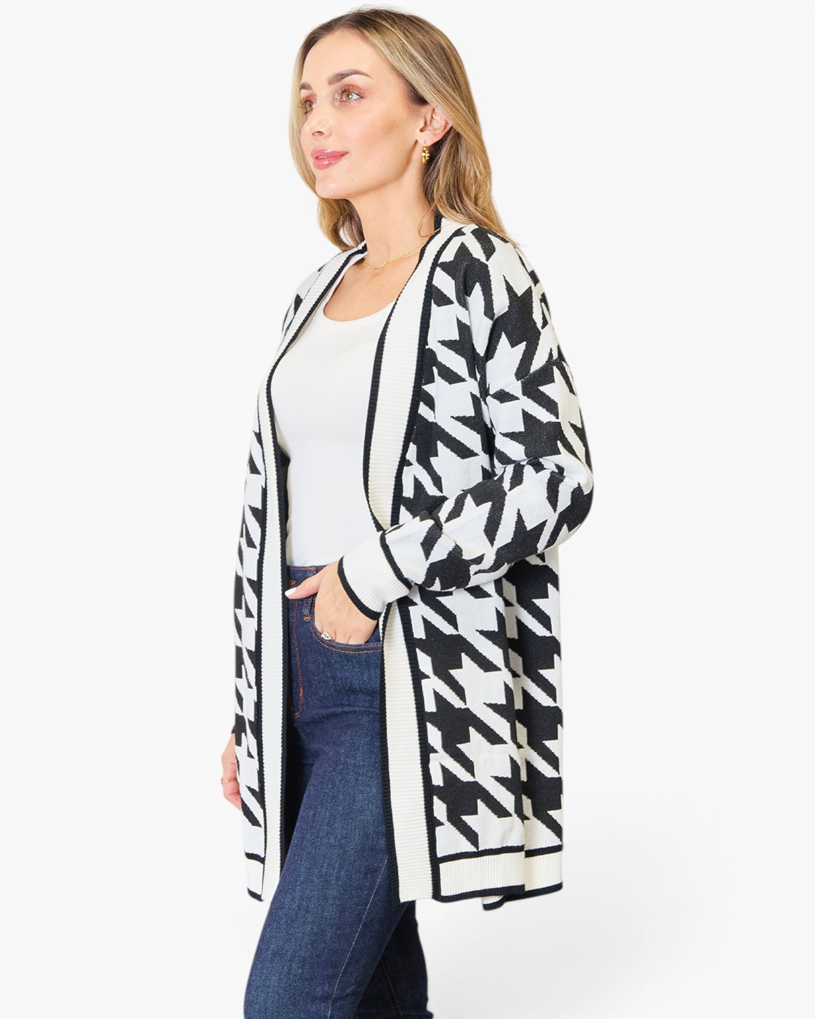 A woman modeling a black and white houndstooth pattern open-front cardigan over a white top and blue jeans, photographed against a plain white studio background.
