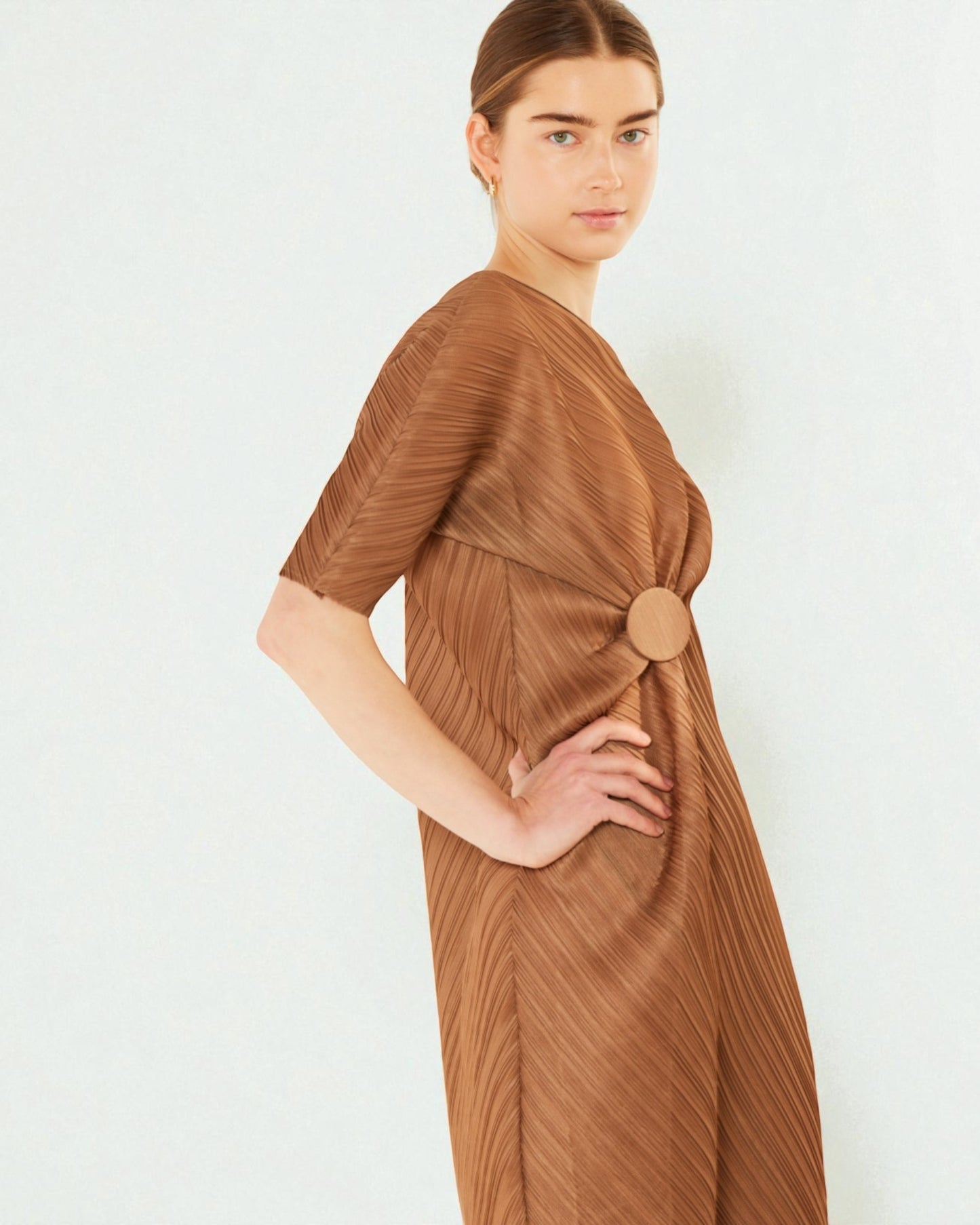 Woman wearing a brown pleated dress with a large button on a white background