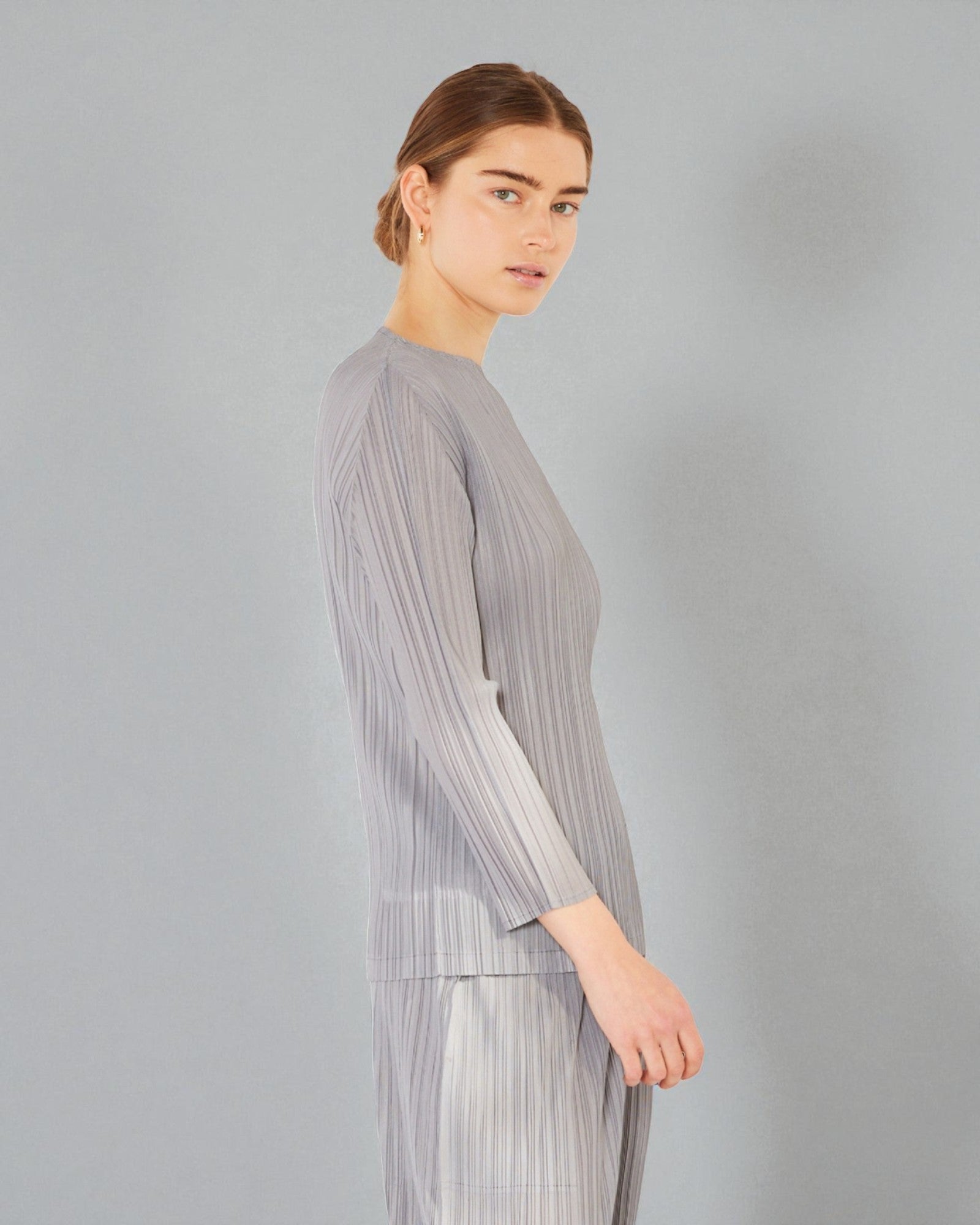 Woman wearing a gray pleated outfit against a plain background