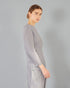 Woman wearing a gray pleated outfit against a plain background