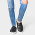 Person wearing ripped blue jeans and black quilted sneakers on a light gray background
