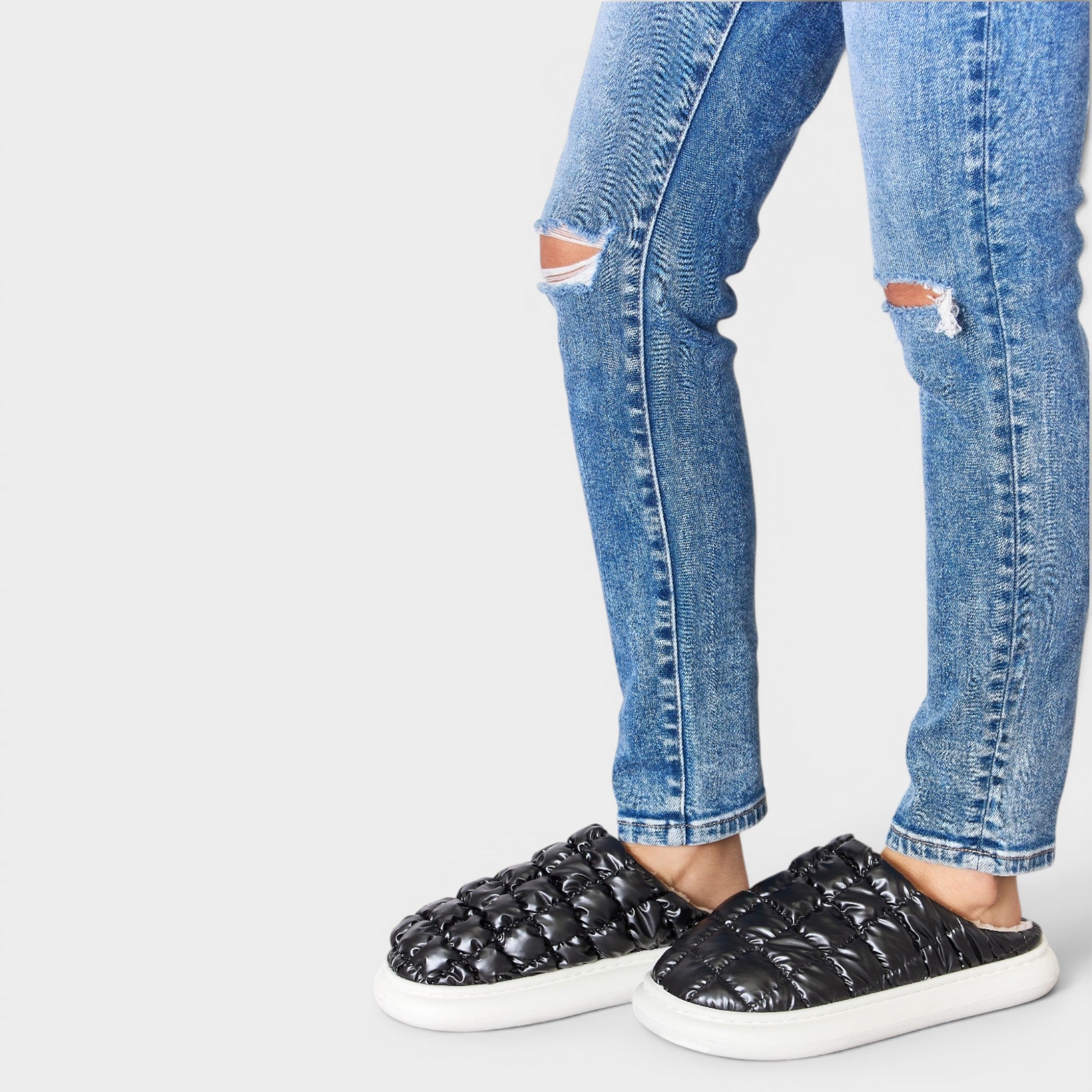 Black slip-on shoes worn with ripped blue jeans on a white background