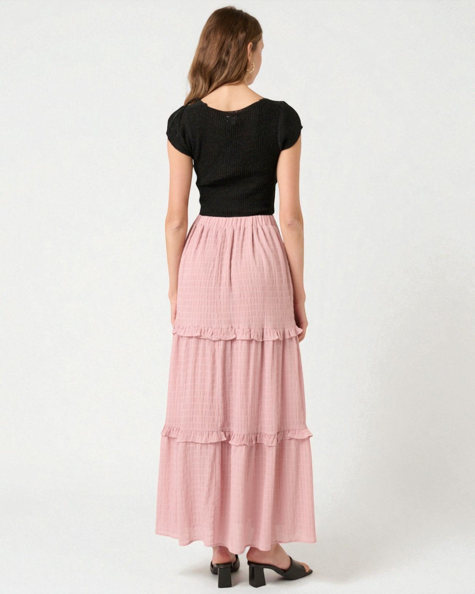 Woman wearing a black top and pink tiered skirt on a white background