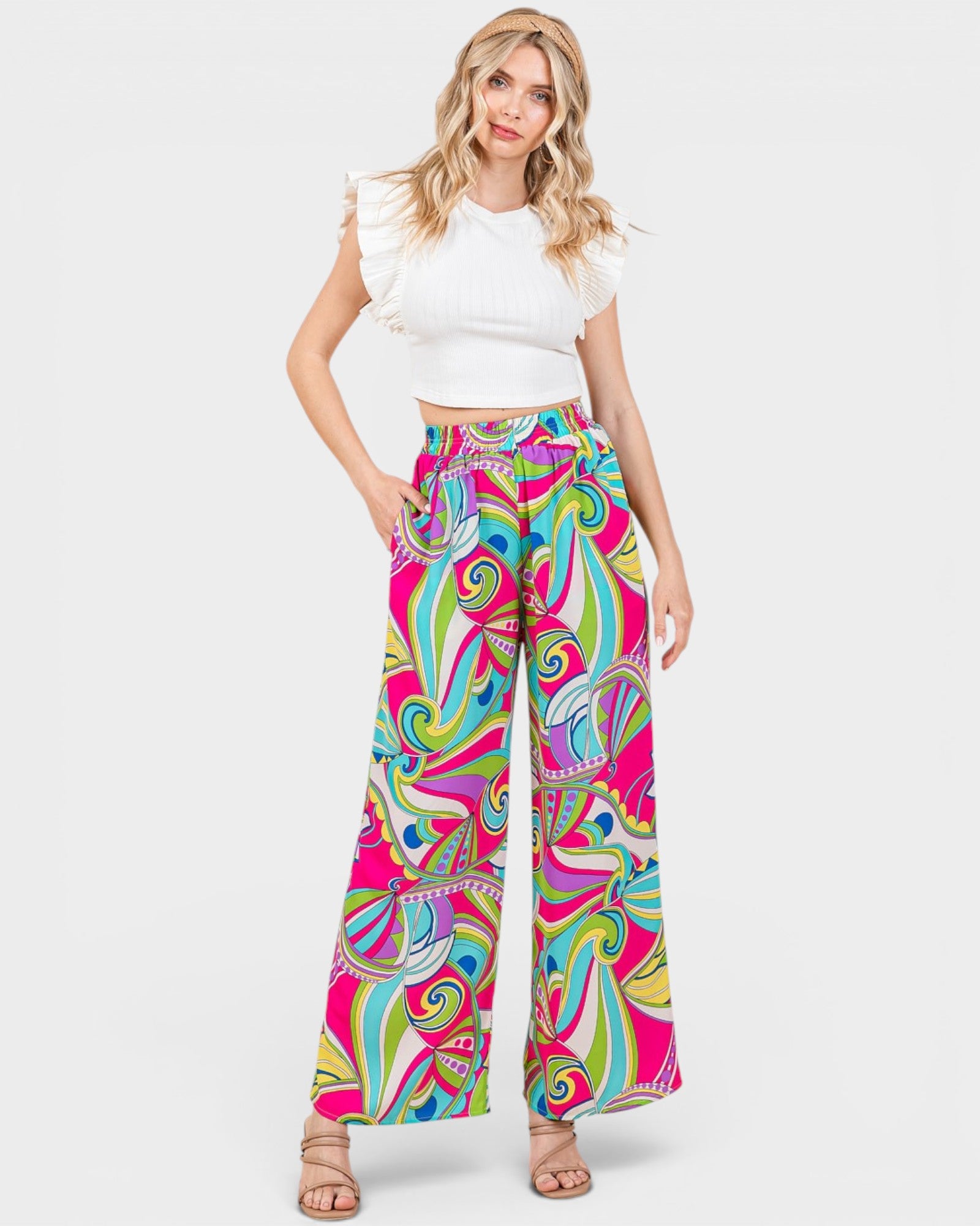 Woman wearing colorful patterned pants and a white top on a white background