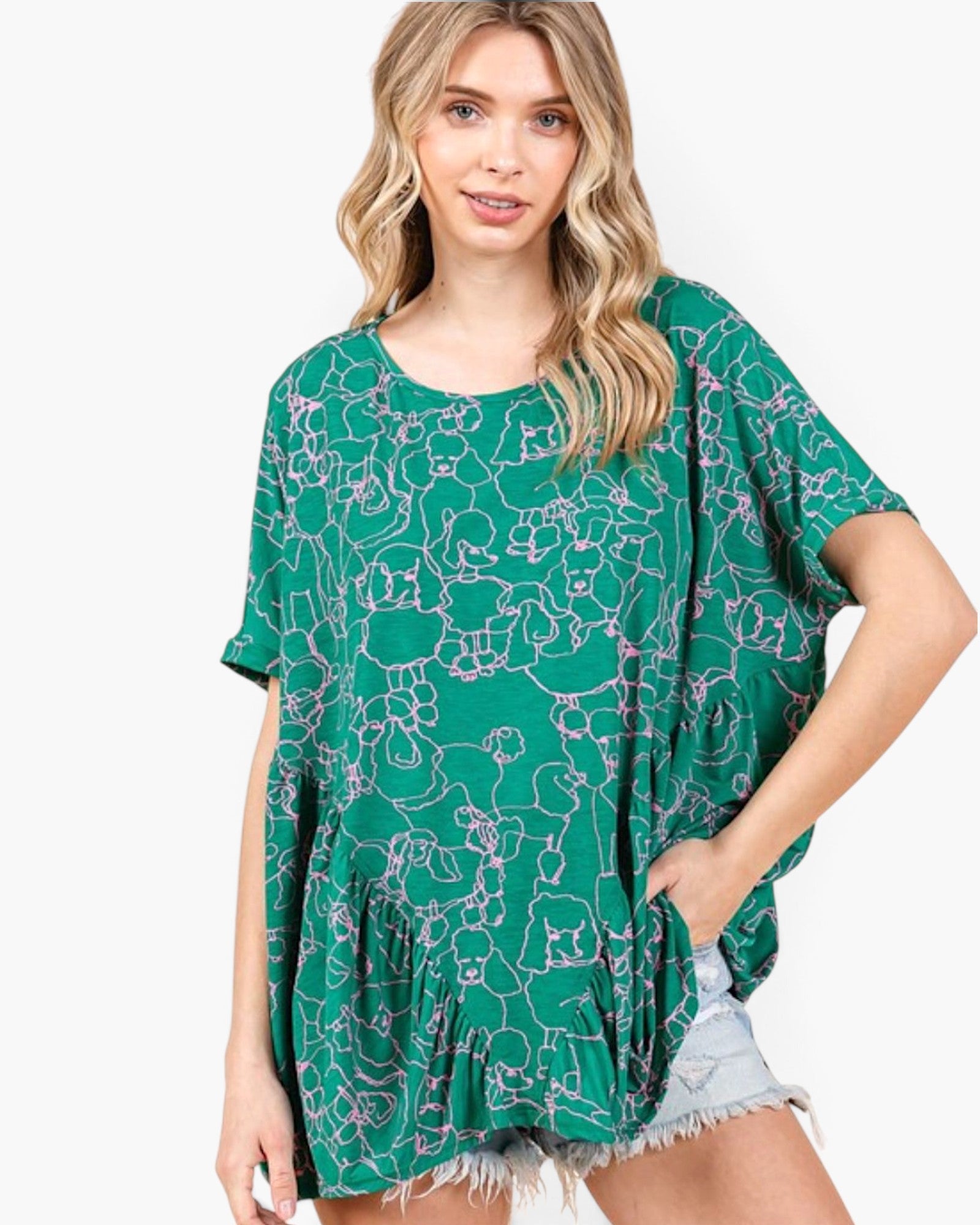 A woman wearing a green short-sleeve tunic top with a white abstract line pattern, paired with light denim shorts, against a plain white background.