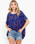 A woman modeling a loose-fitting royal blue short-sleeve top with an orange abstract line pattern, paired with distressed denim shorts, against a plain white background.
