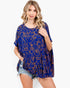 A woman modeling a loose, short-sleeve blue top with an orange abstract line pattern, paired with denim shorts, against a plain white studio background.