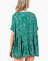 A woman shown from the back wearing a green short-sleeve tunic dress with a white line-art dog pattern and a ruffled hem, set against a plain white background.