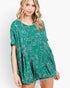 A woman wearing a green short-sleeve tunic top with a white line-art pattern of animals and flowers, featuring a ruffled hem, set against a plain white background.