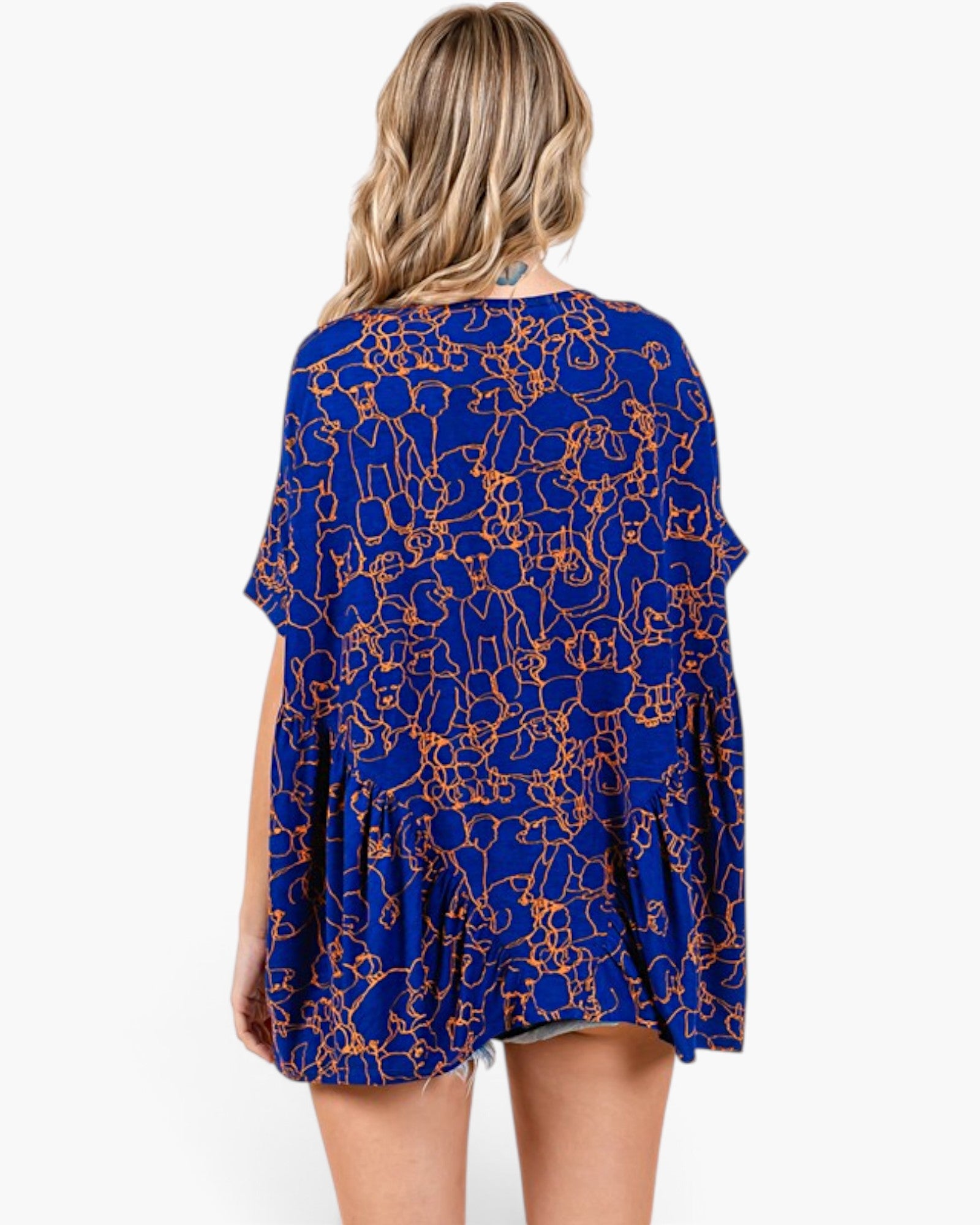 A woman viewed from the back wearing a loose royal blue tunic top with an orange abstract line pattern, set against a plain white background.
