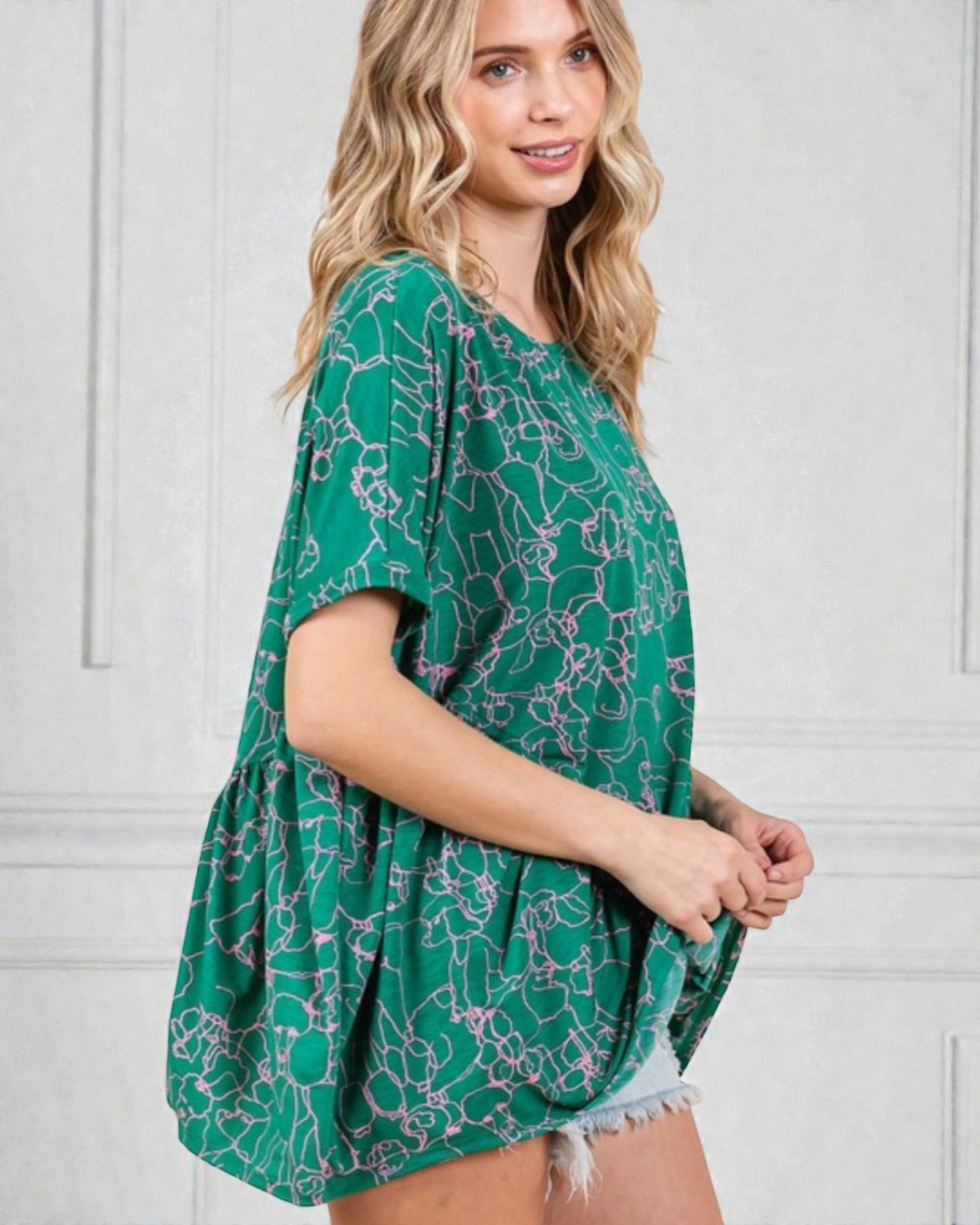 Woman wearing a green patterned top against a white wall
