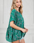 Woman wearing a green patterned top against a white wall