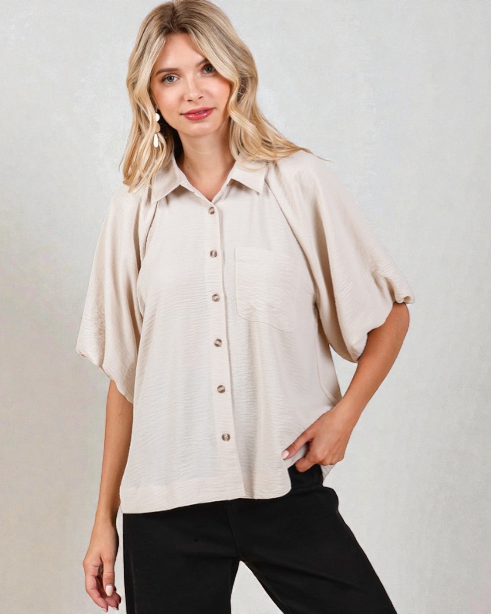 Woman wearing a beige button-up shirt and black pants against a plain background