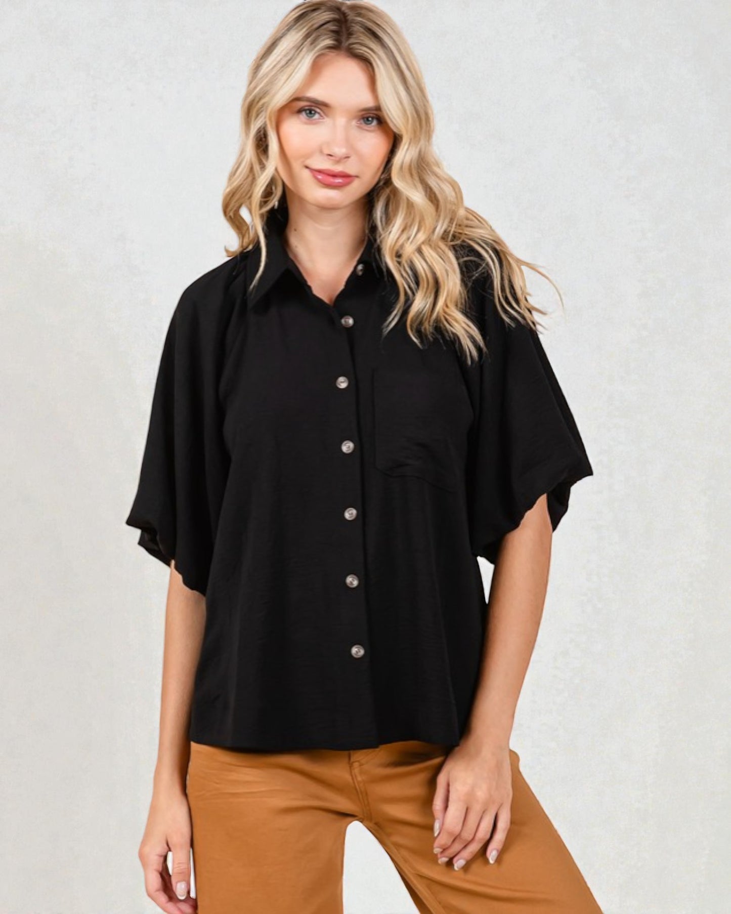 Woman wearing a black short-sleeve blouse with buttons on a light gray background