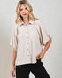 Woman wearing a beige button-up shirt and black pants against a plain background