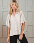 Woman wearing a beige button-up shirt and black pants in front of a neutral-colored door.