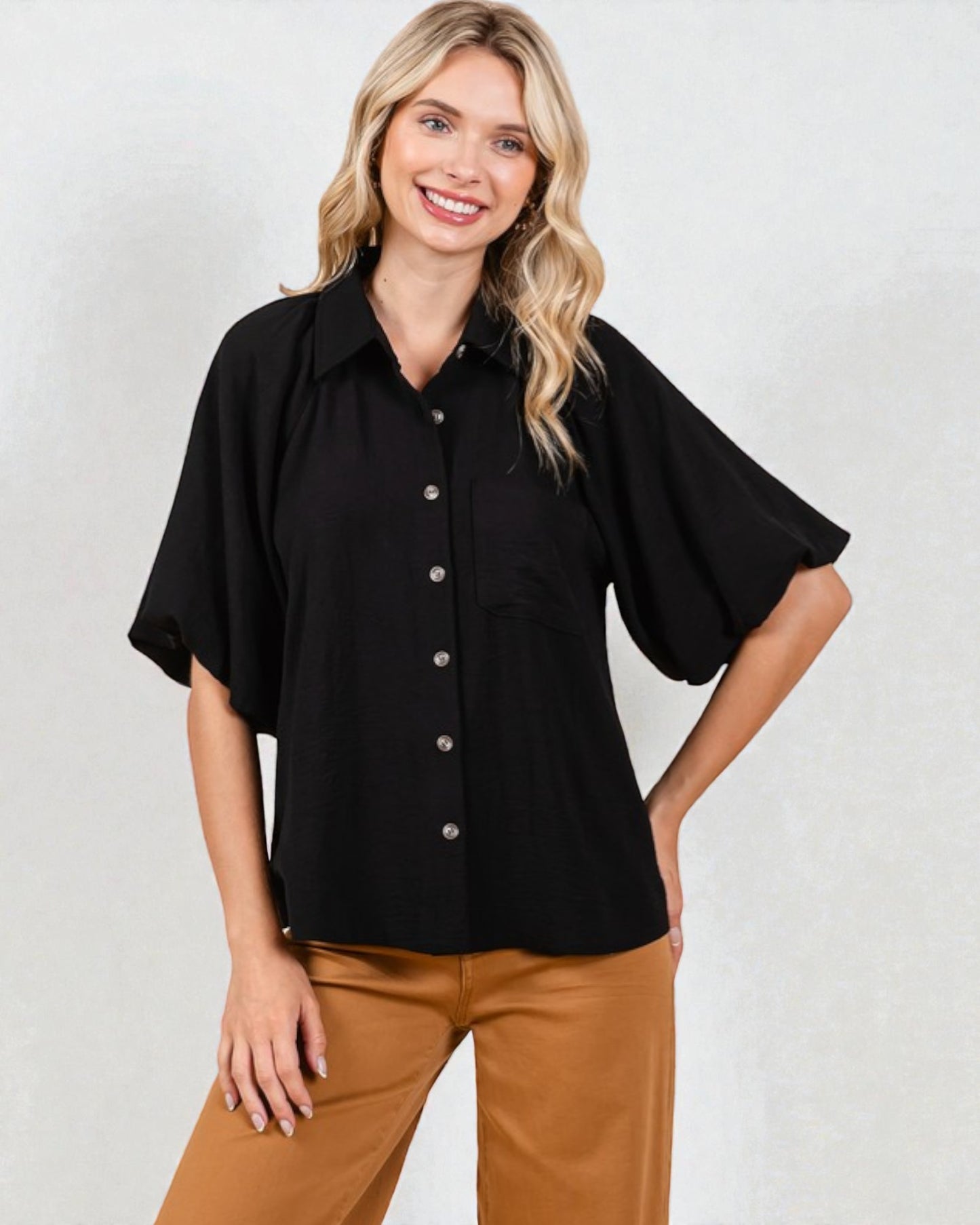 Woman wearing a black blouse with bell sleeves against a white background