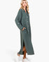 A woman modeling a long-sleeve, button-front midi dress in a muted sage green color, styled with white sneakers against a plain white studio background.