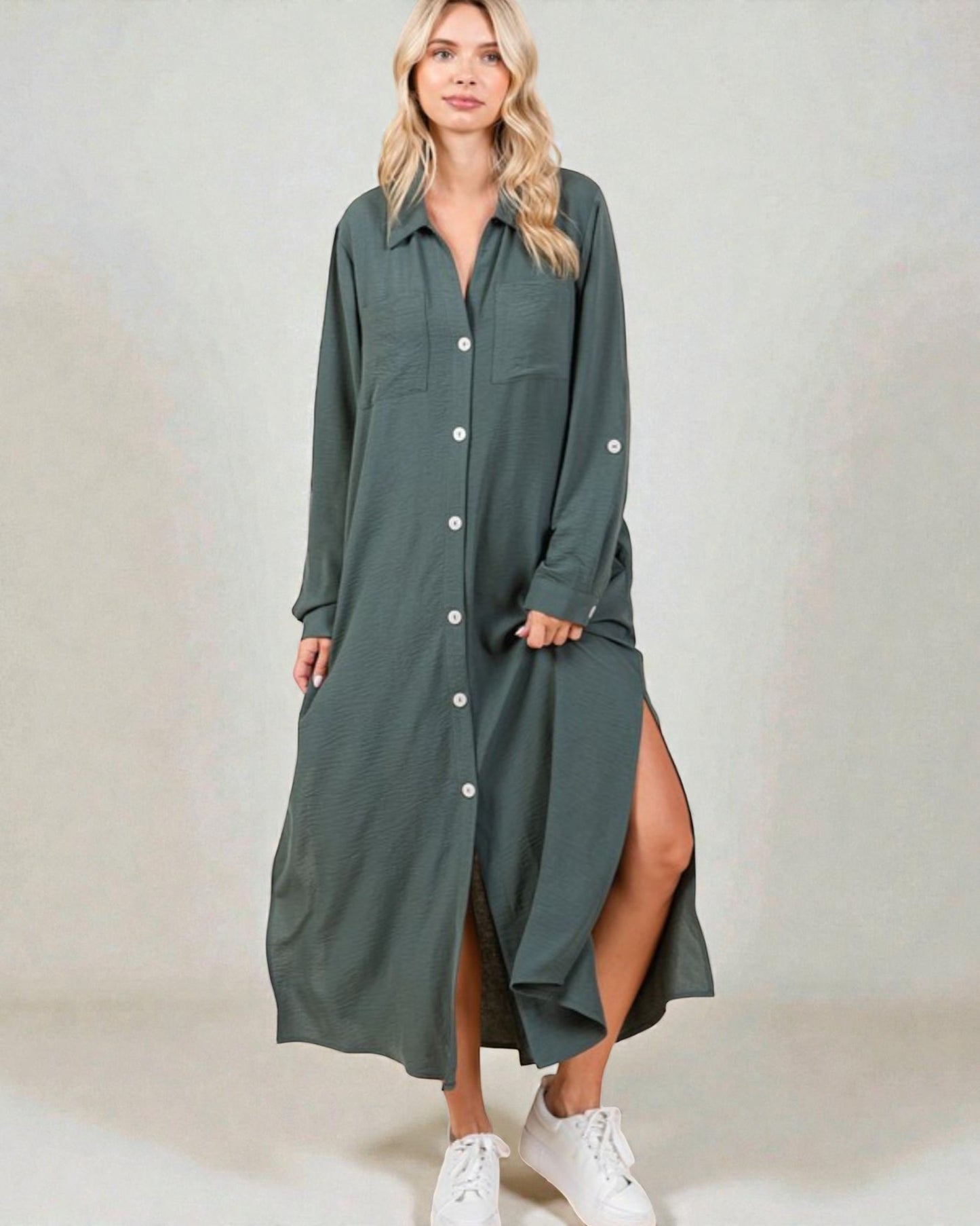 Woman wearing a long green dress with a slit on a plain background