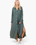 A woman modeling a long-sleeve, button-front midi dress in a muted sage green color, styled with white sneakers against a plain white studio background.