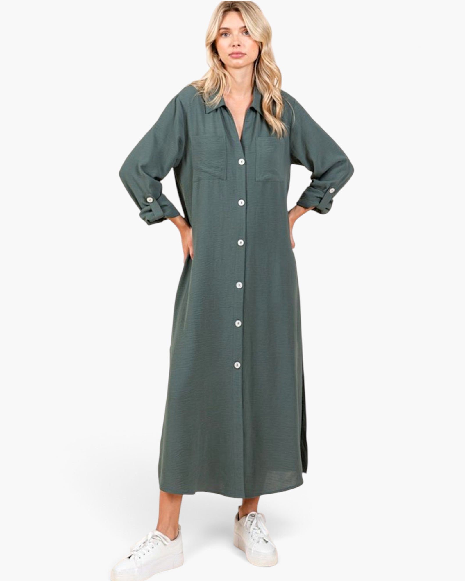 A woman modeling a dark green long-sleeve button-down midi dress with white sneakers, photographed against a clean white studio background.