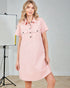 Woman wearing a pink dress with black buttons in a studio setting.