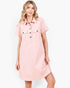 A woman modeling a light pink short-sleeve shirt dress with a button-down front and two chest flap pockets, photographed against a plain light gray studio background.