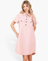 A woman modeling a light pink short-sleeve shirt dress with a button-down front, collar, and chest pockets against a plain white background.